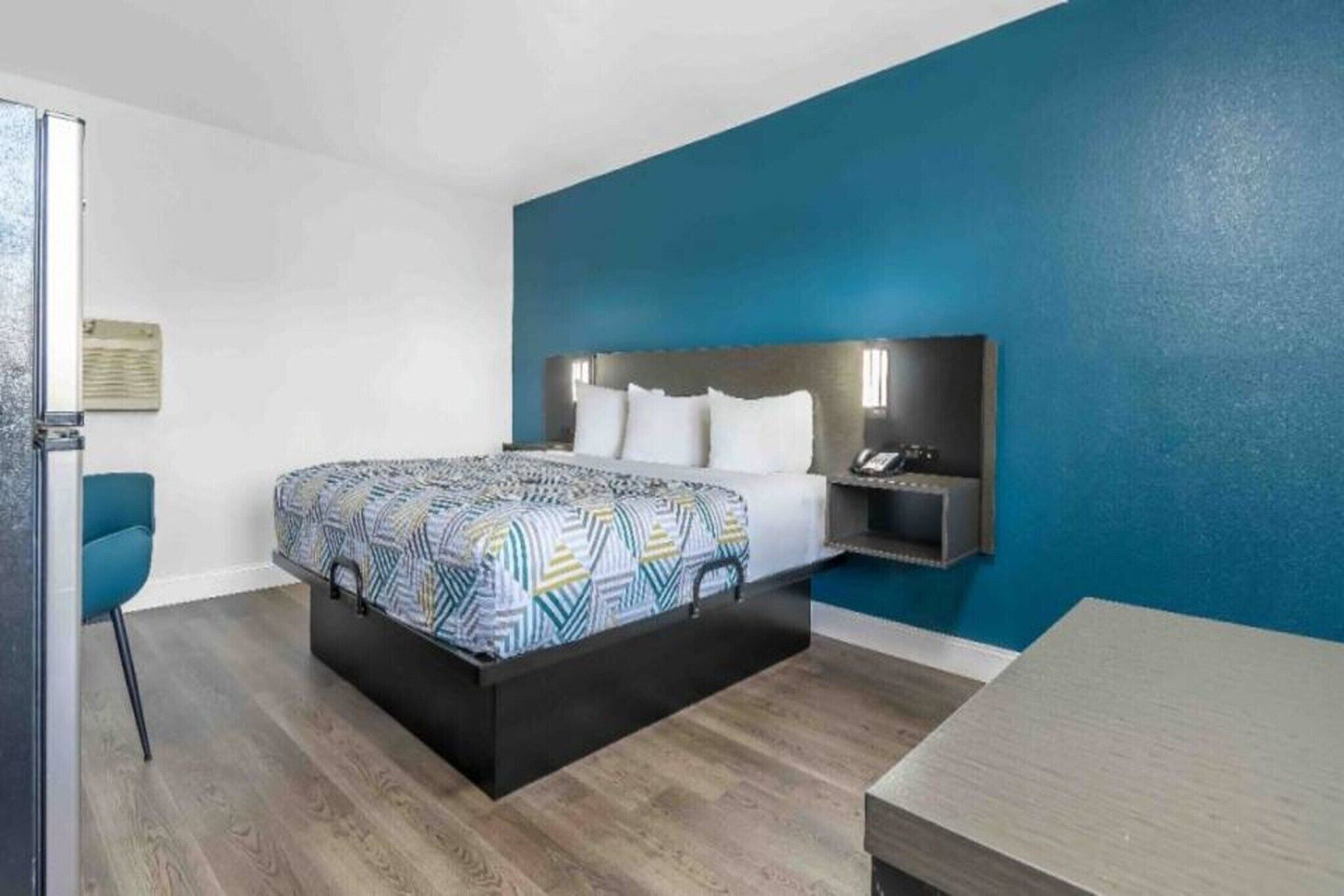 A hotel room with a bed, bedside table, and a chair.