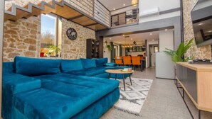 A modern living room with a blue sectional sofa, a kitchen area, and a stone wall. - Villa sa bazenom i jacuzzijem u Dalmatinskoj zagori na 20 min od Splita (Biorine)