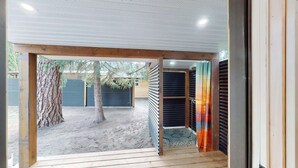 Un pontile in legno conduce a una zona esterna coperta con vista su un albero e un edificio sullo sfondo.