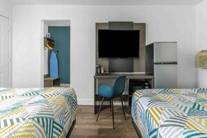 A hotel room with two beds, a desk with a chair, a television, and a refrigerator.