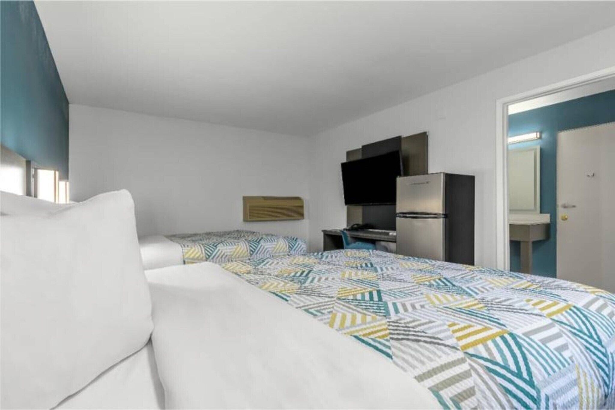 A hotel room with a bed, a desk, a chair, a television, and a door.