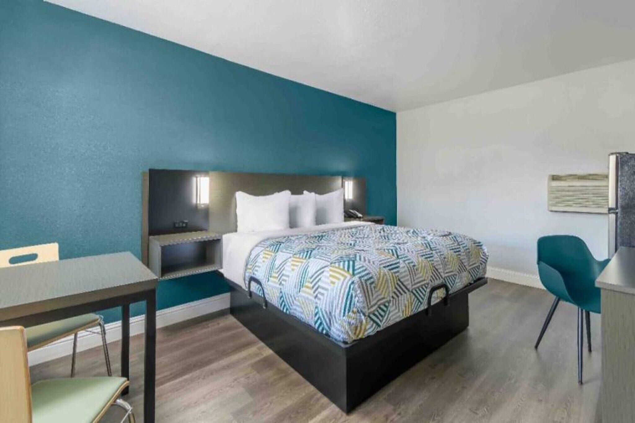 A hotel room with a bed, a desk, a chair, and a nightstand.