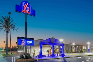 A 6 Suites hotel with a clear entrance sign, a covered outdoor area, and a building with multiple windows.