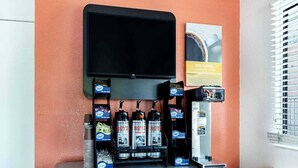 Estação de bebidas com máquina de café, televisão fixada na parede e cartaz publicitário de um produto.