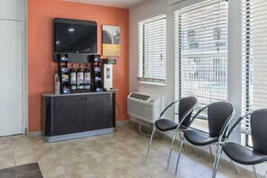 A room with a TV, air conditioning unit, and chairs near a window with blinds.