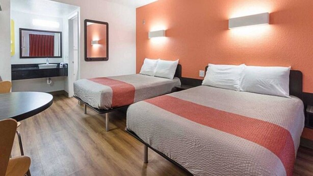 Quarto de hotel com duas camas, uma mesa pequena e banheiro com espelho e pia.