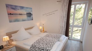 Ein Schlafzimmer mit Bett, Nachttischen, einer Lampe, einem Gemälde und einem Fenster mit Vorhängen.