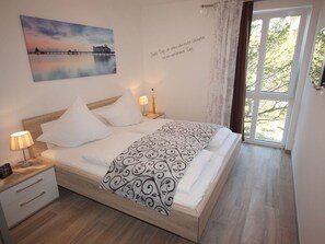 Ein Schlafzimmer mit Bett, Nachttischen, einer Lampe, einem Gemälde und einem Fenster mit Vorhängen.