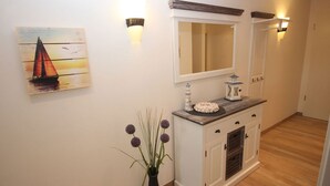 Ein Flur mit Holzboden, einem weißen Schrank mit Spiegel, einer Vase mit violetten Blumen und einem Gemälde eines Segelbootes.
