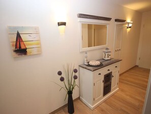 Ein Flur mit Holzboden, einem weißen Schrank mit Spiegel, einer Vase mit violetten Blumen und einem Gemälde eines Segelbootes.
