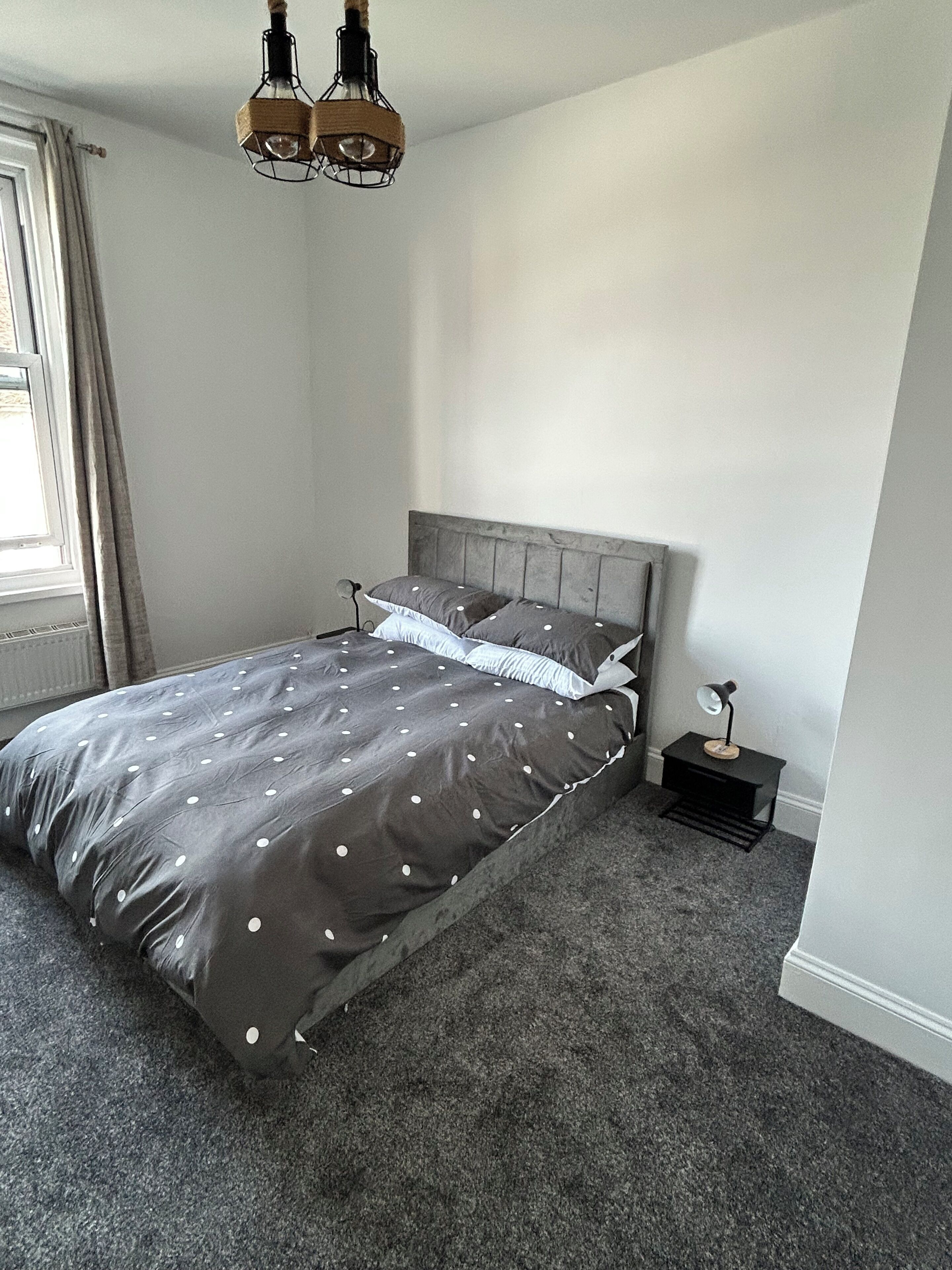 A bedroom with a bed, a nightstand, a lamp, and a hanging light fixture.