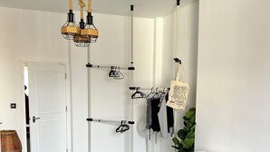 Ein modernes Schlafzimmer mit einem grauen Bett mit weißen Punkten, einem weißen Schreibtisch mit einem Laptop, einem Hängekorbstuhl, einem Ventilator und einem Kleiderständer.