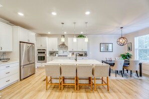 Une cuisine moderne avec des meubles blancs, des appareils en acier inoxydable et un îlot central doté de chaises.