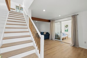 Eine Treppe mit Holzboden und weißen Geländern führt zu einem Raum mit einem blauen Sofa und einer Glastür, die nach draußen führt.
