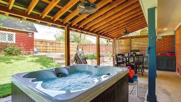 Eine überdachte Terrasse mit Whirlpool, Holzbalken, einer Backsteinwand und einem Essbereich.