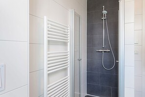 Une salle de bain avec un porte-serviettes blanc, une douche équipée d’un pommeau de douche amovible et des murs carrelés.