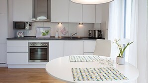 Una cocina moderna con armarios blancos, un microondas, una estufa y una mesa de comedor con un mantel individual colorido.