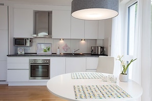 A modern kitchen with white cabinetry, a microwave, a stove, and a dining table with a colorful placemat. - Villa Amelie, App. Baltic Sea - with sea view (Sassnitz)