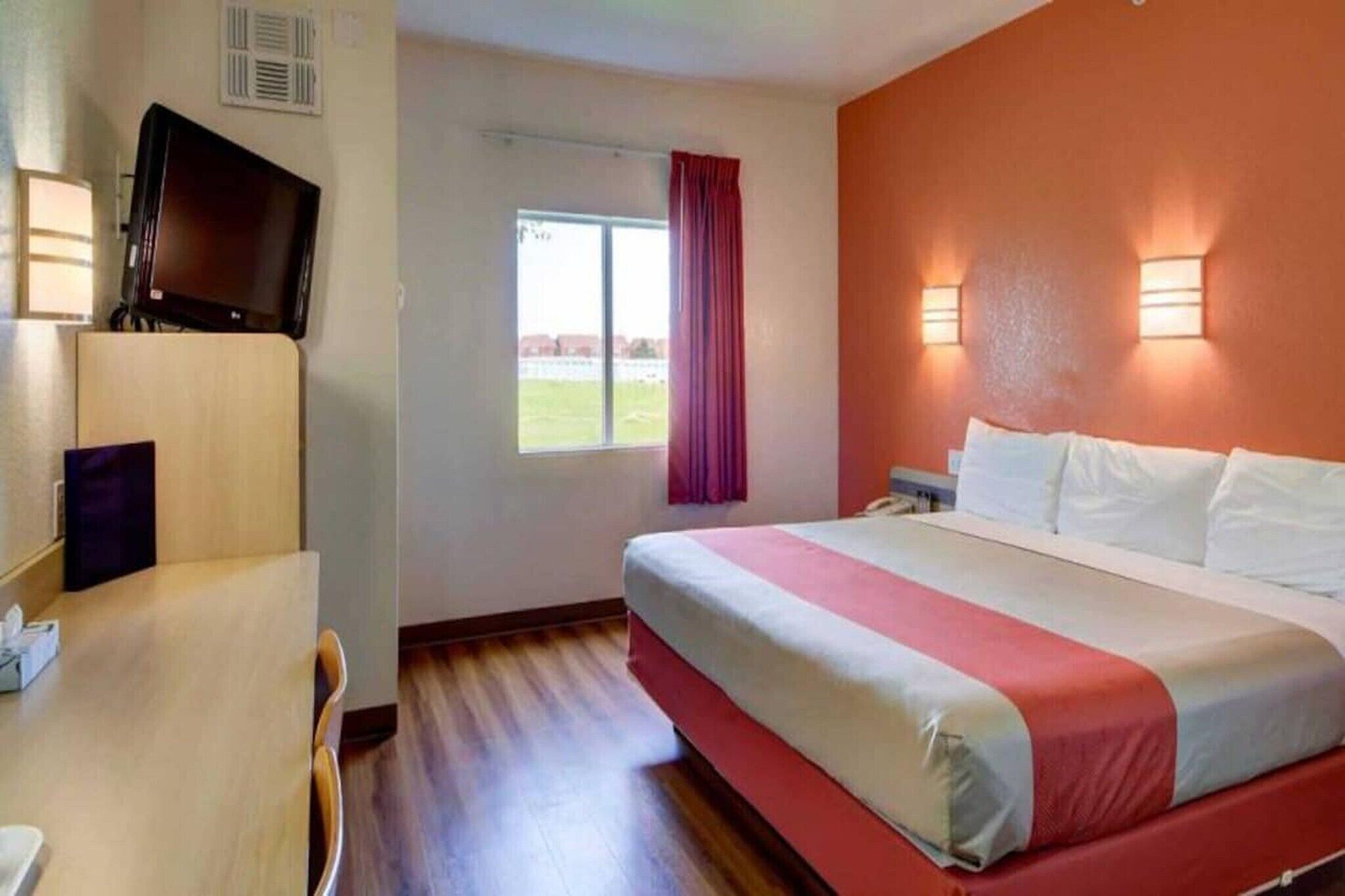 Ett hotellrum med en säng, ett skrivbord, en tv och ett fönster med gardiner.
