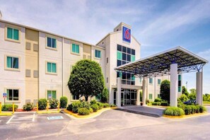 A hotel with a covered entrance, multiple windows, and a parking lot.