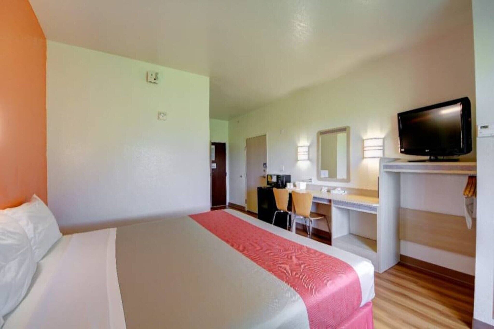 Una habitación de hotel con cama, escritorio, silla, televisor y espejo.