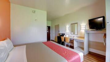 Una habitación de hotel con cama, escritorio, silla, televisor y espejo.