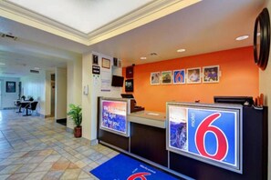 A hotel reception area with a reception desk, a digital display, and a sign indicating the hotel name.