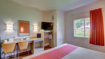 Habitación de hotel con cama, escritorio, sillas, televisión y ventana con cortinas.