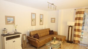 Un salon avec un canapé marron, une table basse en verre, un meuble blanc et des tableaux encadrés accrochés au mur.