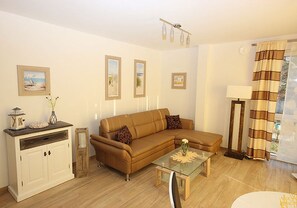 A living room with a brown sofa, a glass coffee table, a white cabinet, and framed pictures on the wall. - Villa Amelie, App. Seagull - with balcony and sea view (Sassnitz)