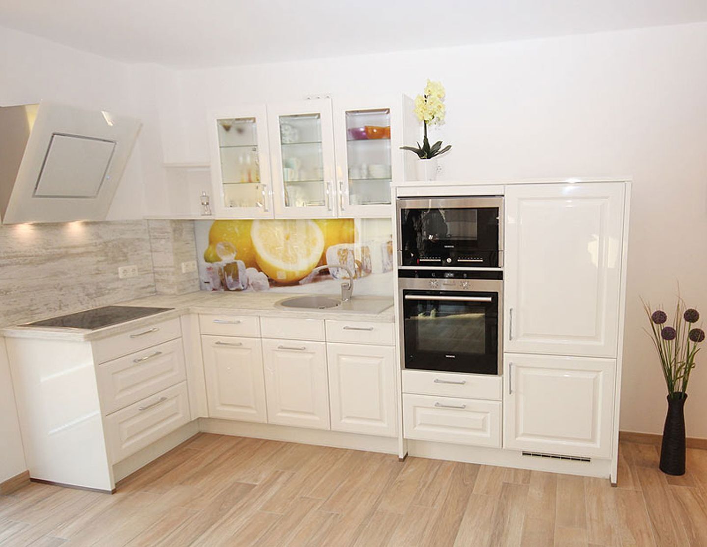 A modern kitchen with white cabinetry, a built-in oven, and a backsplash with a citrus design.