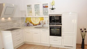 Une cuisine moderne avec des meubles blancs, un four encastré et un revêtement mural décoré de motifs d’agrumes.