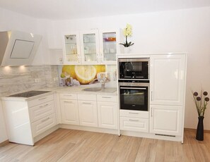 A modern kitchen with white cabinetry, a built-in oven, and a backsplash with a citrus design. - Villa Amelie, App. Seagull - with balcony and sea view (Sassnitz)