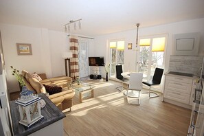 A modern living room with a sofa, coffee table, TV, and dining area. - Villa Amelie, App. Seagull - with balcony and sea view (Sassnitz)