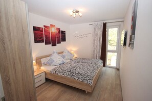 A bedroom with a wooden bed, a nightstand, a wall-mounted lamp, and a window with curtains. - Villa Amelie, App. Seagull - with balcony and sea view (Sassnitz)