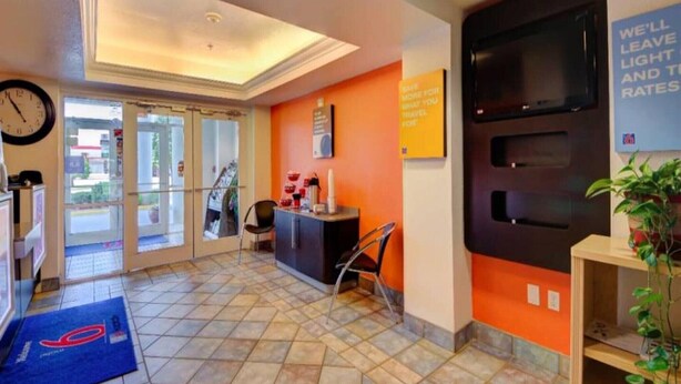 Un hall d’hôtel avec un comptoir d’accueil, une horloge, une plante et un panneau indiquant les tarifs pour le chauffage et la climatisation.
