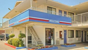 Een hotel met een 'WELCOME' bord, een overdekte ingang, een trap en een parkeerplaats.