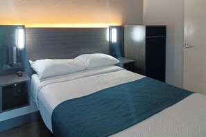 Hotellihuone, jossa on sänky, yöpöydät, vaatekaappi ja seinään kiinnitetyt lamput.