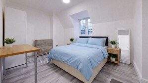 Ein Schlafzimmer mit Bett, Nachttischen, Schreibtisch, Fenster und Tür.