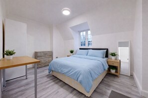 A bedroom with a bed, bedside tables, a desk, a window, and a door. - Discover this spacious living space King’s Cross (London)
