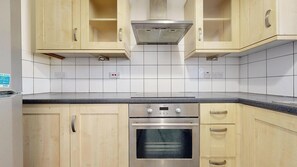 Eine Küche mit hellen Holzschränken, einem Edelstahlbackofen und einer schwarzen Arbeitsplatte.