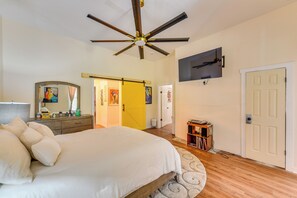 Une chambre à coucher avec un lit, un ventilateur de plafond, un téléviseur fixé au mur et une porte.