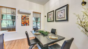 Een eetruimte met een tafel voor vier personen, twee ingelijste kunstwerken aan de muur en een raam met jaloezieën.