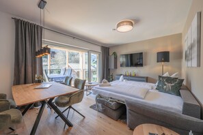 Ein modernes Hotelzimmer mit einem Holzesstisch, einer Couch, einem Bett mit Fernseher und einem Balkon mit Aussicht.