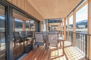 Eine Terrasse im Freien mit Tischen und Stühlen, großen Fenstern und Blick auf die Landschaft.