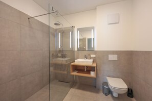 Ein modernes Badezimmer mit einer Duschkabine, einem Waschbecken mit Spiegel darüber und einer Toilette.