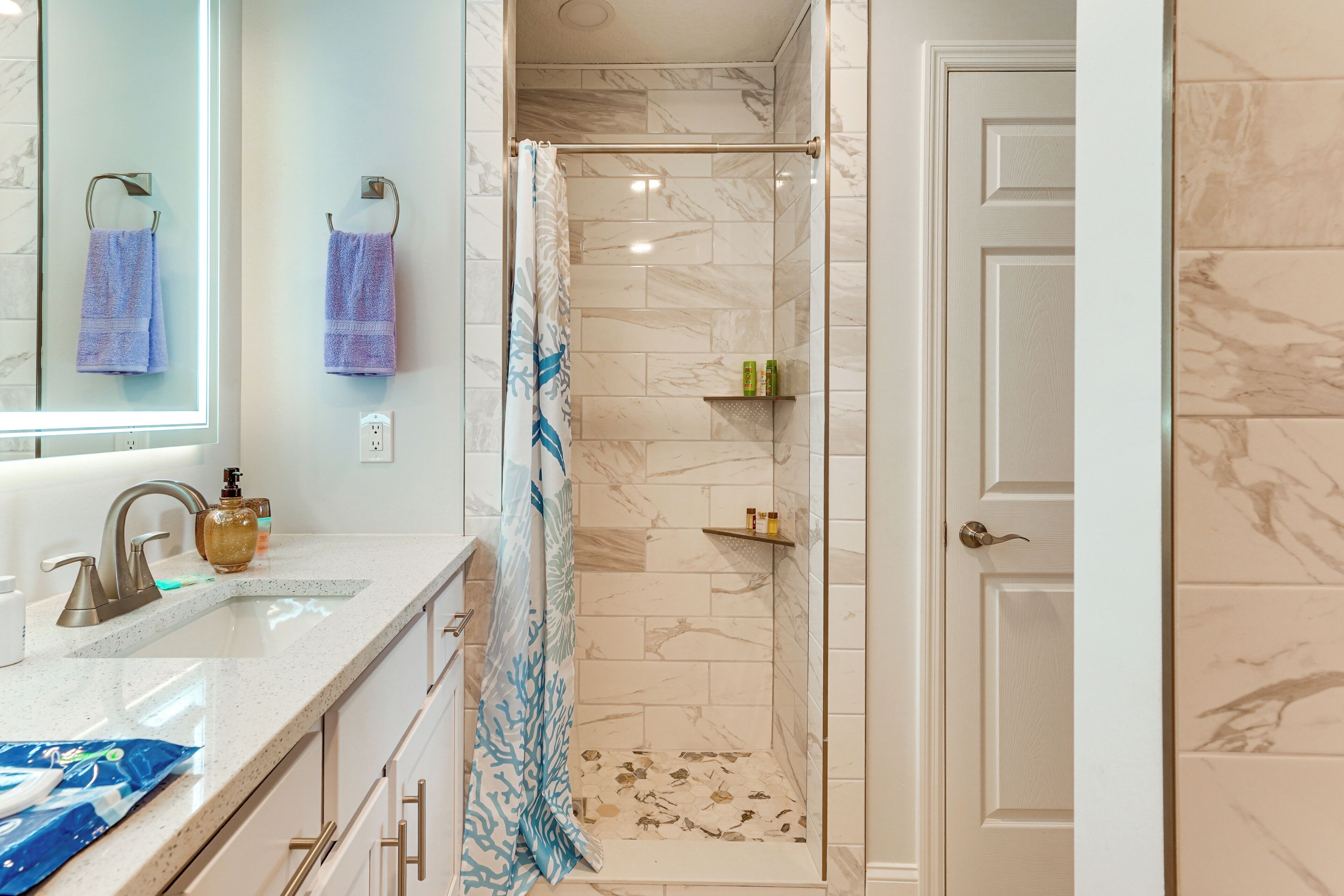 A bathroom with a shower, a sink with a mirror, and a door leading to another room.