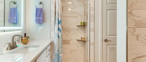 A bathroom with a shower, a sink with a mirror, and a door leading to another room.