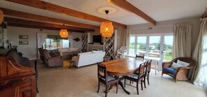 A spacious living area with a wooden dining table, sofas, and wicker chairs.