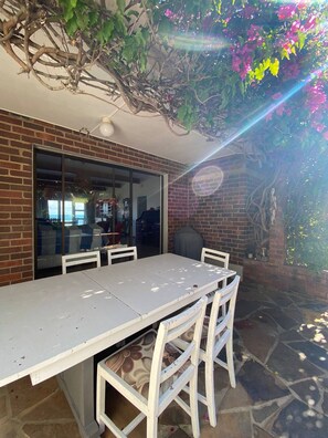 A patio with a table and chairs, a brick wall, and a glass door leading to an interior space. - Serene Coastal Retreat with Private Pool in Amatola (Amatola Coastal)